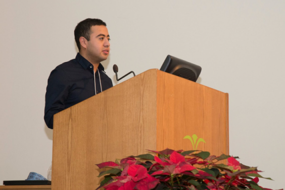 Oscar Herrera at a podium, both facing right. Red flowers in the foreground.