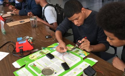 Two students working at desk with what appears to be electrical wire they they are testing or soldering.